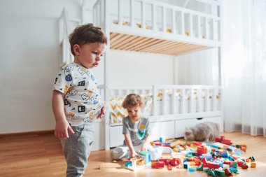 Two little boys have fun indoors in the bedroom with plastic construction set.