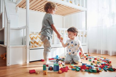 Two little boys have fun indoors in the bedroom with plastic construction set.