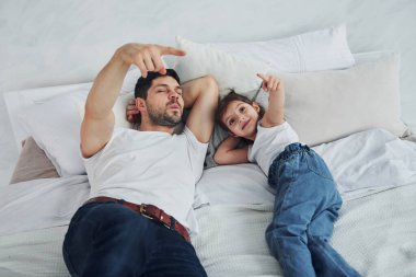 Happy father with his daughter spending free time at home together. Lying down on bed.