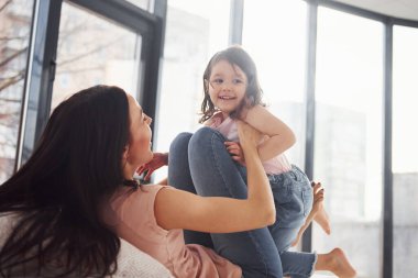Young mother with her daughter spending weekend together on bed.