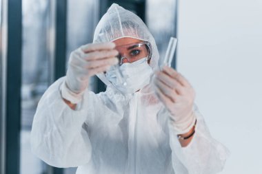 Test tüpleri tutuyor. Laboratuvar önlüklü, koruyucu gözlüklü ve maskeli kadın doktor portresi..