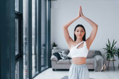 Yoga egzersizleri yapıyor. Spor kıyafetleri içinde ince vücutlu genç bir kadın evde spor yapıyor..