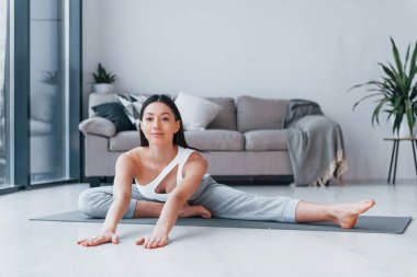 Yoga egzersizleri yapıyor. Spor kıyafetleri içinde ince vücutlu genç bir kadın evde spor yapıyor..