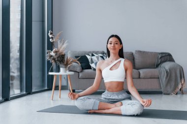 Yoga egzersizleri yapıyor. Spor kıyafetleri içinde ince vücutlu genç bir kadın evde spor yapıyor..