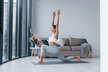 Esnek egzersizler yapıyor. Spor kıyafetleri içinde ince vücutlu genç bir kadın evde spor yapıyor..