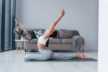 Esnek egzersizler yapıyor. Spor kıyafetleri içinde ince vücutlu genç bir kadın evde spor yapıyor..