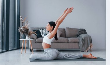 Esnek egzersizler yapıyor. Spor kıyafetleri içinde ince vücutlu genç bir kadın evde spor yapıyor..