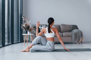 Spor kıyafetleri içinde ince vücutlu genç bir kadın evde spor yapıyor..