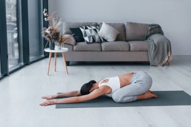 Esnek egzersizler yapıyor. Spor kıyafetleri içinde ince vücutlu genç bir kadın evde spor yapıyor..