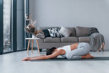 Esnek egzersizler yapıyor. Spor kıyafetleri içinde ince vücutlu genç bir kadın evde spor yapıyor..