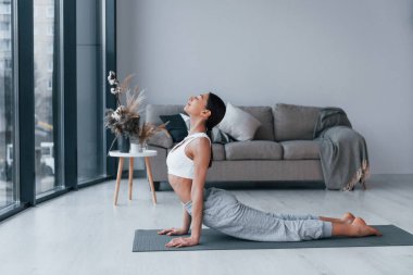 Esnek egzersizler yapıyor. Spor kıyafetleri içinde ince vücutlu genç bir kadın evde spor yapıyor..