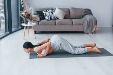 Esnek egzersizler yapıyor. Spor kıyafetleri içinde ince vücutlu genç bir kadın evde spor yapıyor..