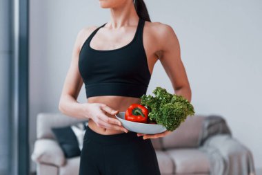 Sağlıklı yiyecekleri ellerinde tutuyor. Siyah spor giyimli zayıf vücutlu genç bir kadın evde spor salonuna gidiyor..