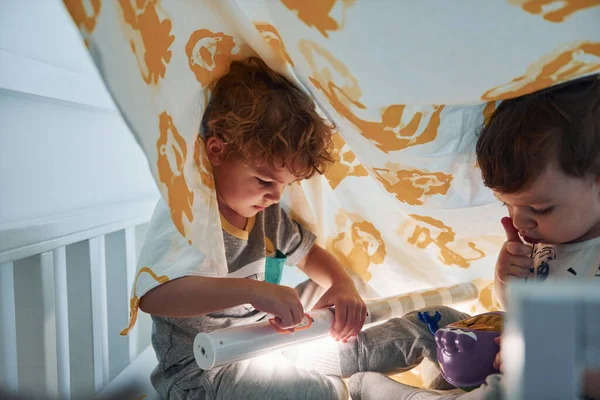 İki küçük çocuk dinleniyor ve battaniyenin altında birlikte eğleniyorlar..