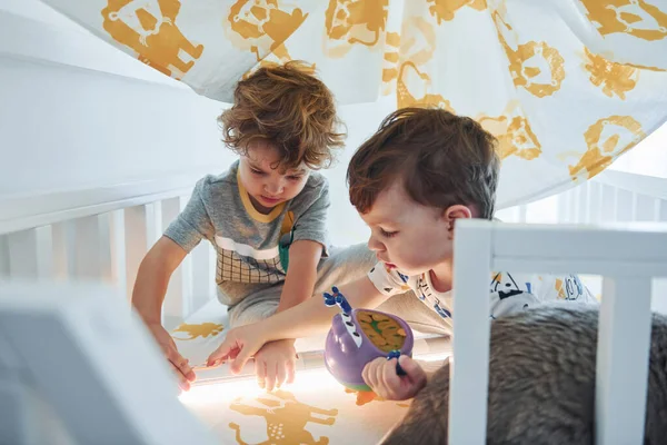 İki küçük çocuk dinleniyor ve battaniyenin altında birlikte eğleniyorlar. Kedi uzanıyor..