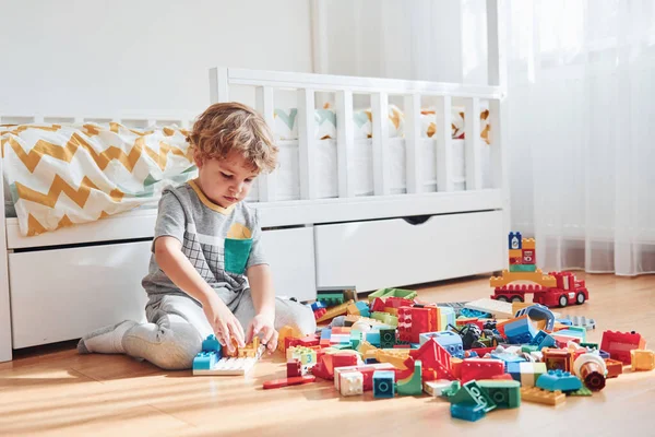 Şirin küçük çocuk içeride plastik inşaat setiyle oturuyor ve eğleniyor..