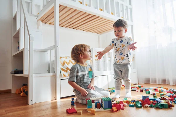 Two little boys have fun indoors in the bedroom with plastic construction set.