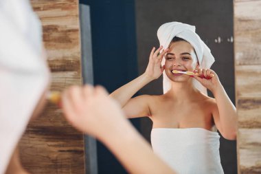 Beautiful young woman standing in bathroom near the mirror and brushing her teeth.