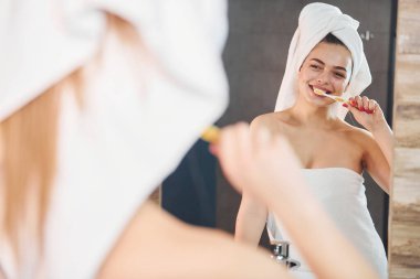 Beautiful young woman standing in bathroom near the mirror and brushing her teeth.