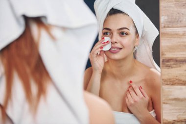 Güzel genç bir kadın banyoda dikiliyor, aynaya bakıyor ve yüzüne bakıyor..