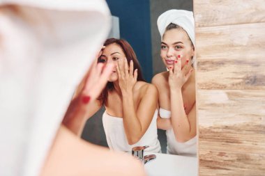 İki güzel genç kadın aynanın yanında banyoda dikiliyor ve yüzlerini temizliyorlar..