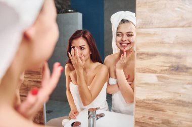 İki güzel genç kadın aynanın yanında banyoda dikiliyor ve yüzlerini temizliyorlar..