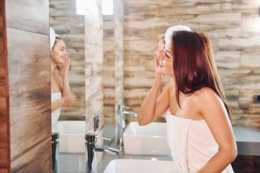 Two beautiful young women standing in bathroom near the mirror together and cleaning their faces.