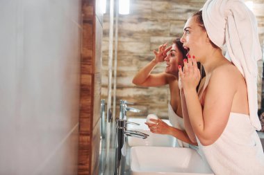İki güzel genç kadın aynanın yanında banyoda dikiliyor ve yüzlerini temizliyorlar..