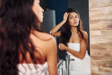 Güzel genç bayan aynanın yanında banyoda duruyor..