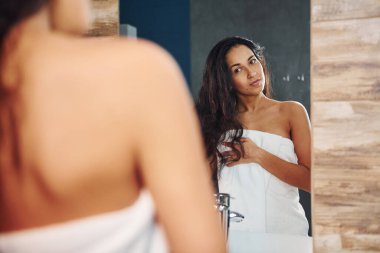 Beautiful young woman standing in bathroom near the mirror.