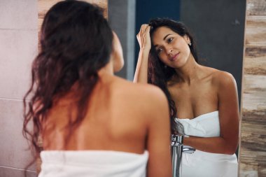 Güzel genç bayan aynanın yanında banyoda duruyor..