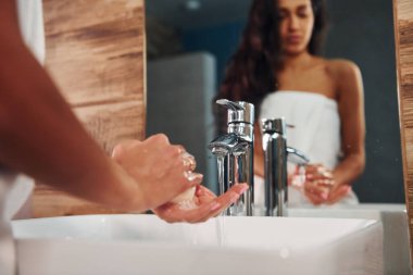 Güzel esmer kadın banyoda aynanın yanında duruyor ve ellerini yıkıyor..