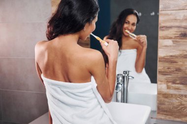 Güzel, genç bir esmer aynanın yanında duruyor ve dişlerini fırçalıyor..