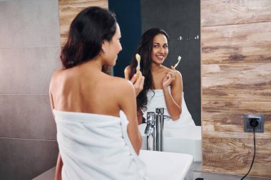 Güzel, genç bir esmer aynanın yanında duruyor ve dişlerini fırçalıyor..