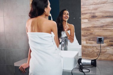 Güzel, genç bir esmer aynanın yanında duruyor ve dişlerini fırçalıyor..