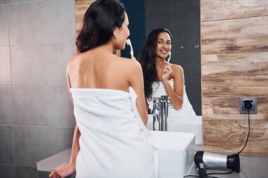 Güzel, genç bir esmer aynanın yanında duruyor ve dişlerini fırçalıyor..