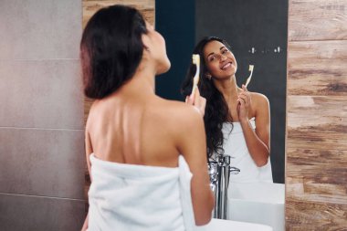 Güzel, genç bir esmer aynanın yanında duruyor ve dişlerini fırçalıyor..