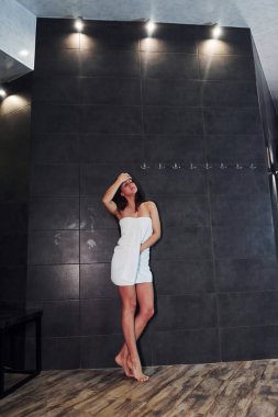 Sıska vücutlu, beyaz havluyla kaplıca duşunda duran güzel esmer..