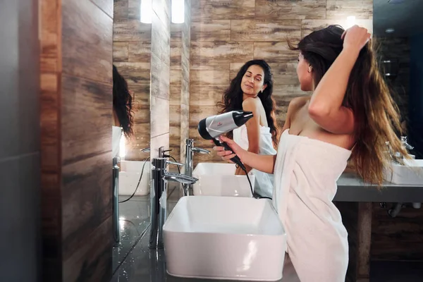 İki güzel genç kadın aynanın yanında durmuş, yüzlerini temizliyor ve saçlarını kurutuyorlar..