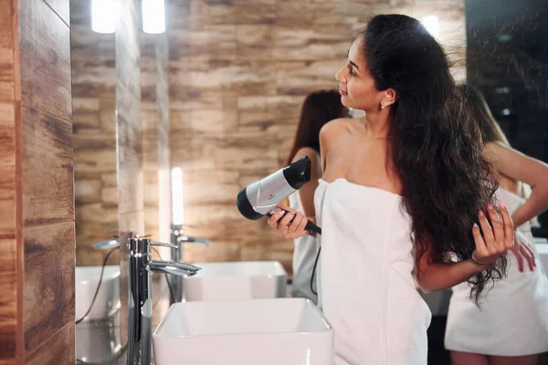İki güzel genç kadın aynanın yanında durmuş, yüzlerini temizliyor ve saçlarını kurutuyorlar..