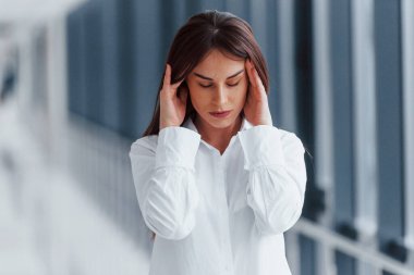 Modern havaalanında ya da koridorda beyaz gömlekli esmer bir kadın gün ortasında baş ağrısı çekiyor..