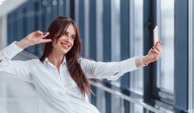 Beyaz gömlekli esmer, modern havaalanında ya da gündüz vakti koridorda selfie çekiyor..
