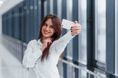 Brunette in white shirt that walks indoors in modern airport or hallway at daytime.