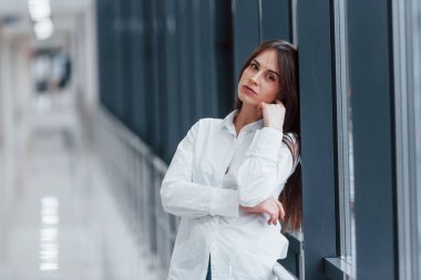 Brunette in white shirt indoors in modern airport or hallway at daytime.