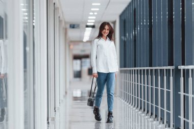 Gündüz vakti modern havaalanında ya da koridorda yürüyen beyaz gömlekli esmer kadın..