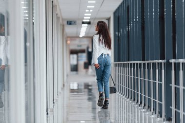 Beyaz gömlekli esmer, modern havaalanında ya da gündüz vakti koridorda yürüyor..