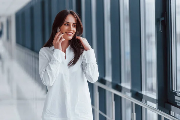 Brunette White Shirt Indoors Talking Phone Modern Airport Hallway Daytime — стоковое фото