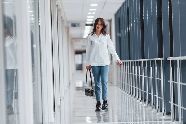 Beyaz gömlekli esmer, modern havaalanında ya da gündüz vakti koridorda yürüyor..