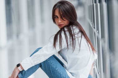 Beyaz gömlekli esmer, modern havaalanında ya da gündüz vakti koridorda oturuyor..