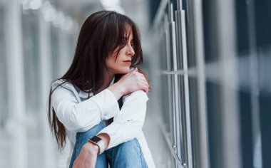 Beyaz gömlekli esmer, modern havaalanında ya da gündüz vakti koridorda oturuyor..